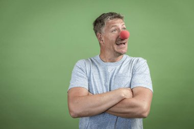 Kırmızı palyaço burunlu ve yeşil arka planda gri gömlekli adam.