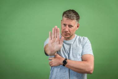 Gri tişörtlü, gri saçlı orta yaşlı bir adam yeşil arka planda poz veriyor.