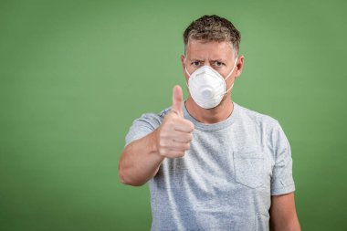 Fffp2 burunlu ve ağız maskeli adam yeşil arka planın önünde duruyor.