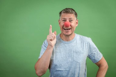 Kırmızı palyaço burunlu ve yeşil arka planda gri gömlekli adam.