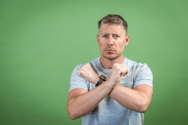 Gri tişörtlü, gri saçlı orta yaşlı bir adam yeşil arka planda poz veriyor.