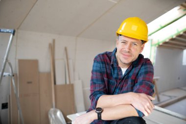 İnşaat alanındaki sarı kasklı adam alçıpan inşaatında çalışıyor.