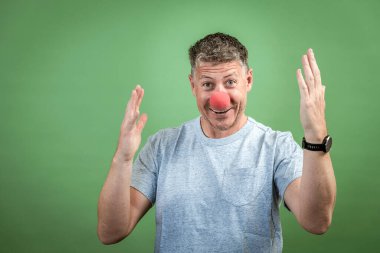 Kırmızı palyaço burunlu ve yeşil arka planda gri gömlekli adam.