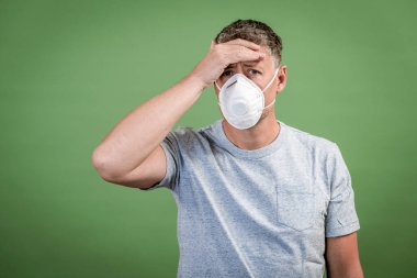 Fffp2 burunlu ve ağız maskeli adam yeşil arka planın önünde duruyor.