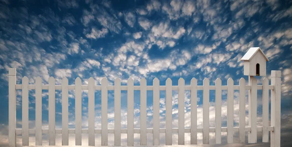 Recinzione bianca con uccello casa e cielo blu — Foto Stock