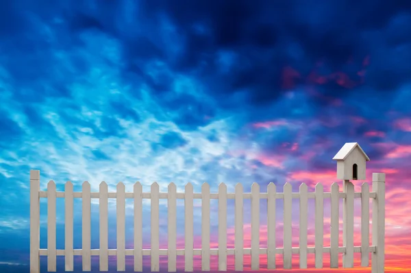 Kuş evi ve mavi gökyüzü ile beyaz çit — Stok fotoğraf