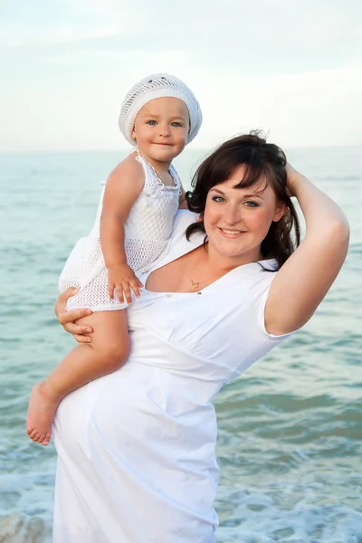 Jonge zwangere vrouw met haar dochter op het strand. — Stockfoto