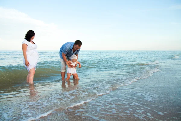 Zwangere en gelukkige familie met een dochter op het strand. — Stockfoto