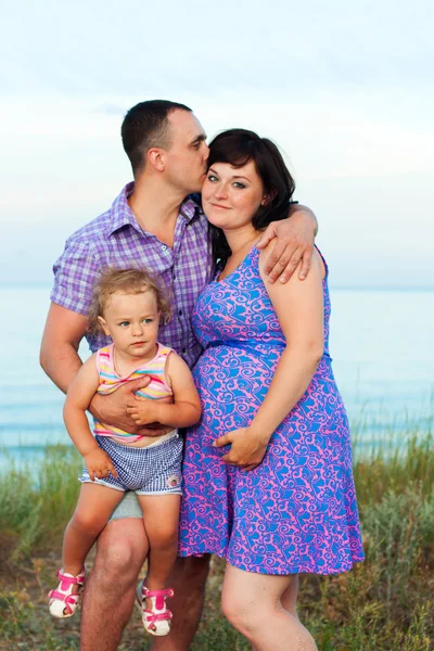 Zwangere en gelukkige familie met een dochter op het strand. — Stockfoto