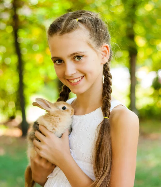 Roztomilá holčička s králíkem v zahradě. — Stock fotografie