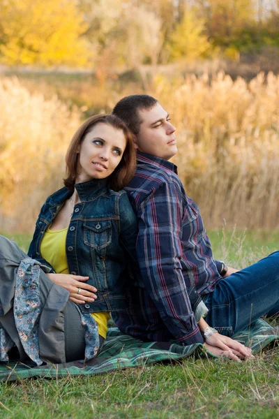 Loving couple sitting on the grass in the autumn garden. — Stock Photo, Image