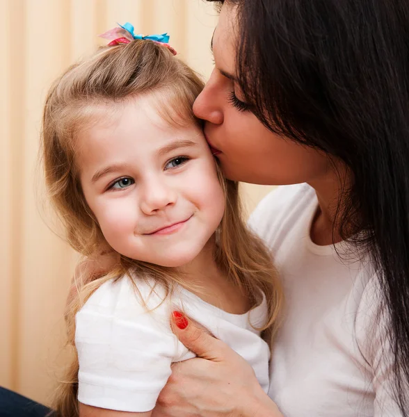 Young mother is kissing her small daughter. — Stock Photo, Image