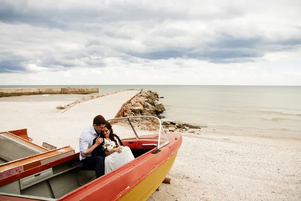 Stijlvolle pasgetrouwden zitten in een boot op het strand. — Stockfoto