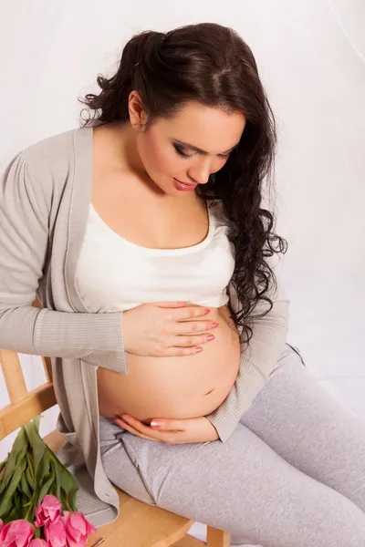 Schöne schwangere Frau mit Tulpen im Inneren. — Stockfoto