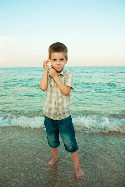 Petit garçon avec une coquille sur la plage du soir . — Photo