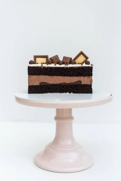 用奶油海绵蛋糕装饰的巧克力蛋糕 白色底座上站着一块饼干 孤立的背景 为孩子们的生日宴会准备的美味的食物 糕点工艺 — 图库照片