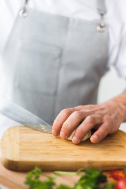 Mutfaktaki aşçı ahşap bir tahtada bıçakla haşlanmış bir yumurtayı dilimliyor. Yumurtaların hazırlanması ve işlemleri. Mutfakta ev atmosferi. Yeşillik ve mutfak malzemelerinin yanına.. 