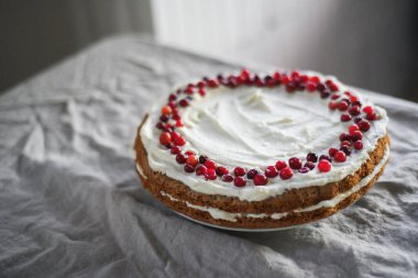Masanın üzerinde beyaz mascarpone kreması ve kızılcıklarla süslenmiş lezzetli bir havuçlu kek duruyor. Her gün için güzel bir tatlı.