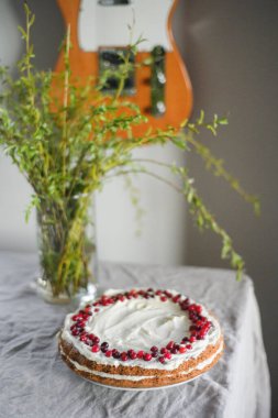 Masanın üzerinde beyaz mascarpone kreması ve kızılcıklarla süslenmiş lezzetli bir havuçlu kek duruyor. Her gün için güzel bir tatlı. Masadaki vazoda yeşiller var. Bahar hala hayat