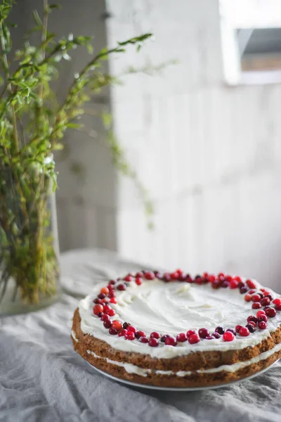 Masanın üzerinde beyaz mascarpone kreması ve kızılcıklarla süslenmiş lezzetli bir havuçlu kek duruyor. Her gün için güzel bir tatlı. Masadaki vazoda yeşiller var. Bahar hala hayat