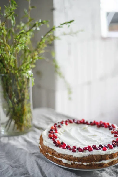 Masanın üzerinde beyaz mascarpone kreması ve kızılcıklarla süslenmiş lezzetli bir havuçlu kek duruyor. Her gün için güzel bir tatlı. Masadaki vazoda yeşiller var. Bahar hala hayat