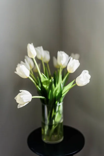 蓝色的桌子上立着一束漂亮的白色郁金香 插在一个透明的花瓶里 后面的轻墙和文字的地方 家庭内部 高质量的照片 — 图库照片