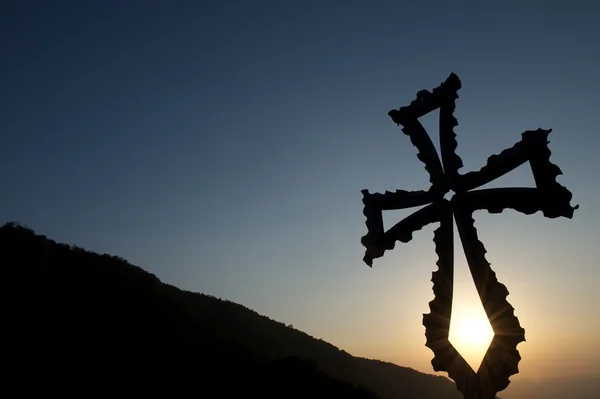 Metalen christelijke kruis bij zonsondergang met bergen op de achtergrond Stockfoto