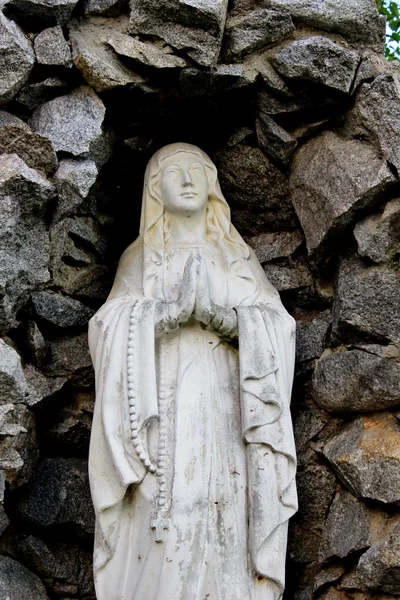 Estátua vintage de uma jovem virgem rezando com um rosário pendurado em seus braços com um fundo de pedras — Fotografia de Stock