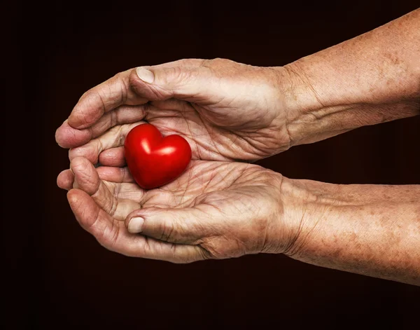 Anciana manteniendo el corazón rojo en sus palmas — Foto de Stock