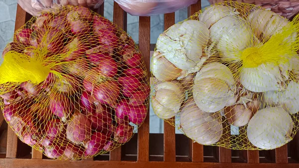 Red and white small onion in net plastic bags on a wooden bar background.