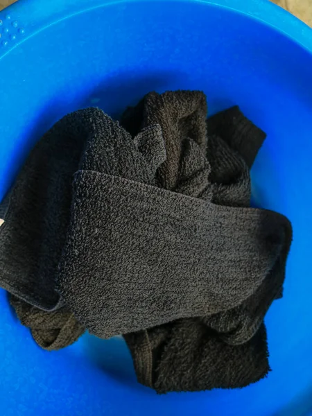 Dirty black towels in a blue basin lying on the floor.