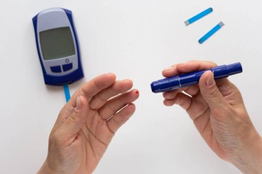 Beyaz arka plandaki glikoz ölçer üzerindeki kan şekerini hesaplamak için üzerinde kan damlası olan kadın elinin üst görünümü