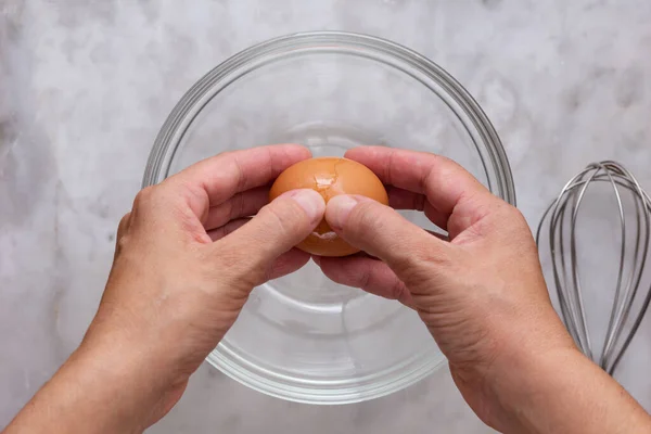Vista dall'alto della donna mano cracking uovo crudo marrone in ciotola di vetro sulla superficie di marmo — Foto Stock