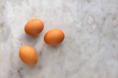 Mermer yüzeyinde kopya alanı olan üç çiğ kahverengi yumurtanın üst görünümü