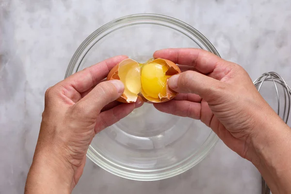大理石の表面に生の茶色の卵をガラスボウルに割れ女性の手のトップビュー — ストック写真