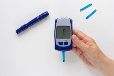 Monitörde E harfi ile el ele tutuşan glukoz sayacının üst görünümü beyaz arkaplanda hata anlamına gelir