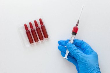 Beyaz arka planda enjeksiyon için B vitamini dolu şırınga fıçısını tutan tıbbi eldivenli kadının üst görüntüsü.