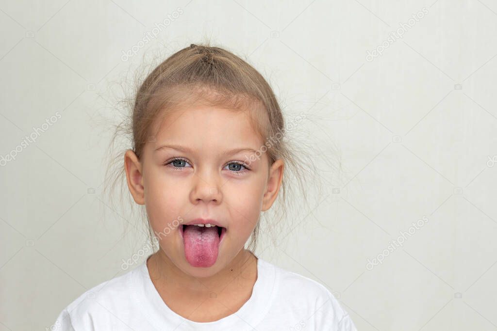 Isolated caucasian funny little girl of 5 years looking at camera and sticking out tongue joyfully on white background