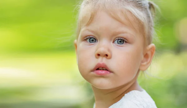 Portrait of serious beautiful little girl of 2 years looking at camera on green blurred background with copy space — Fotografia de Stock
