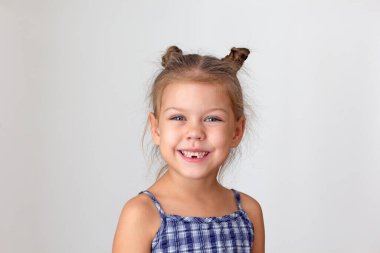 Portrait of happy caucasian child kid little girl of 5 years on grey background looking at camera showing her teeth without lost lower teeth. Concept deciduous teeth