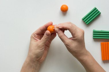 Kadın elleri, polimer kilden portakal meyvesi yaratmak için turuncu topun üzerinde diş çubuğuyla nokta yapıyor.