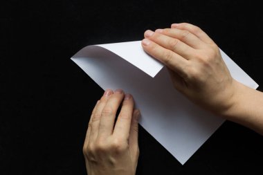 Kadın, siyah arkaplanda kare olması için dikdörtgen kağıt katlıyor.