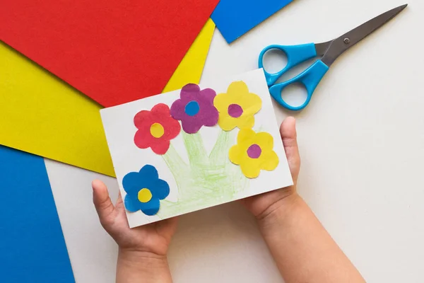 白色背景上印有儿童手中花朵的手工贺卡 — 图库照片