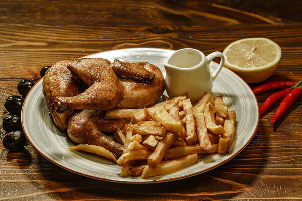 Grilled chicken legs with french fries, chips in plate with lemons and olives. Restaurant food closeup