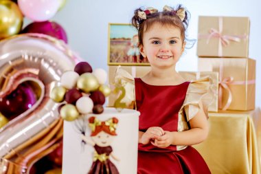 Doğum günü pastasının yanında duran ve kameraya dikkatlice bakan iki yaşında küçük bir kız çocuğu. Güzel bebek doğum günü fotoshop 'u