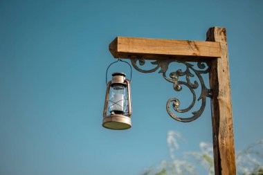 Outdoor low angle view of antique lantern with blue sky background hanging on a pole. Vintage lantern