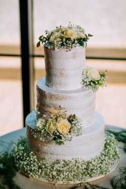 Klas ve zarif beyaz nişan pastası. Pencerelerin önünde doğal çiçekler ve bulanık arkaplan.