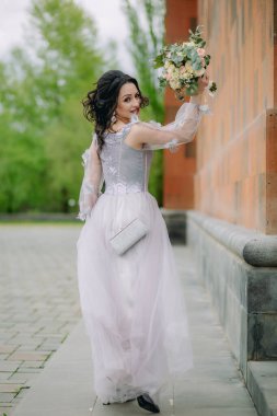 Kilisenin yanında duran zarif elbiseli aktif, gülümseyen nedime buketini gösteriyor. Nedime fotoğrafı.