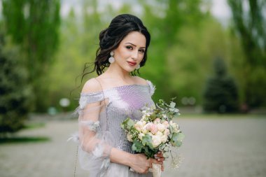 Şirin ve gülümseyen nedime bulanık yeşil arka planda gelin buketi tutuyor ve kameraya bakıyor. Nedime fotoğrafı.