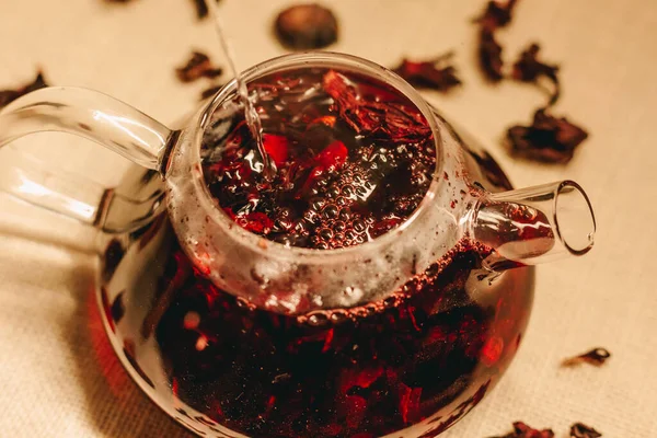 Pouring hot boiling water into the glass teapot. Making pink coloured tea. Warmish tea photoshoot .